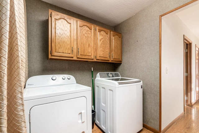 laundry area with a textured ceiling, baseboards, cabinet space, light wood finished floors, and washing machine and clothes dryer