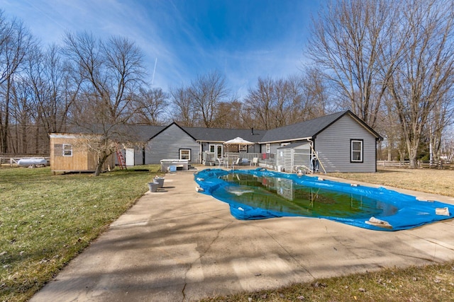 view of pool featuring a wooden deck, a lawn, a covered pool, fence, and an outdoor structure