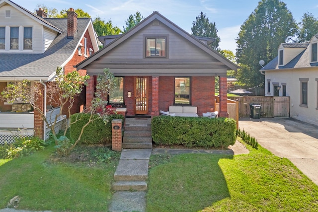 bungalow-style house with a front yard, fence, a porch, and brick siding