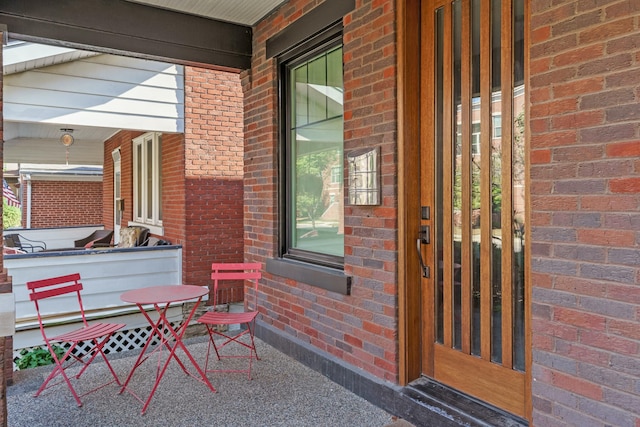 view of exterior entry featuring covered porch and brick siding