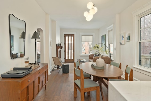 dining space with dark wood-style floors, arched walkways, a notable chandelier, and baseboards