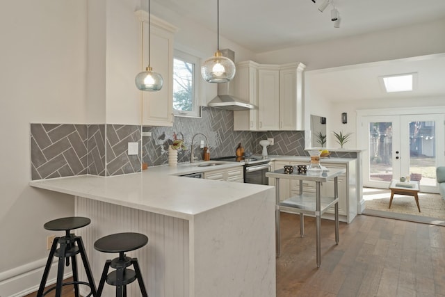 kitchen featuring a peninsula, wood finished floors, a sink, decorative backsplash, and stainless steel electric stove