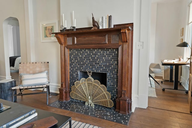 living area featuring arched walkways, a fireplace, wood finished floors, and baseboards