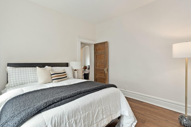 bedroom with arched walkways, baseboards, and wood finished floors