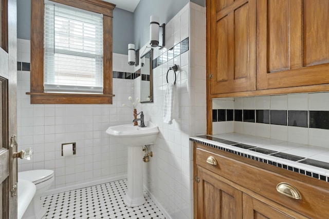 bathroom featuring tile patterned flooring, a sink, tile walls, and toilet