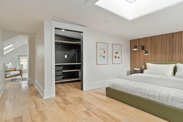 bedroom with a skylight, baseboards, light wood-style floors, a closet, and a walk in closet