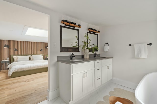 full bath featuring a skylight, marble finish floor, double vanity, a sink, and a freestanding tub