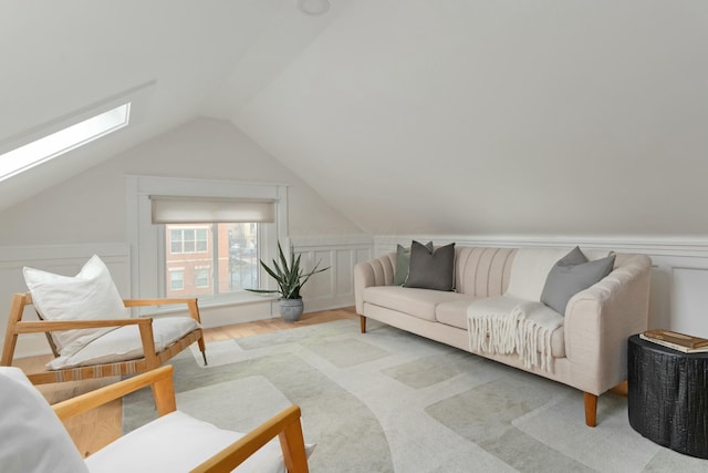 interior space featuring lofted ceiling with skylight, a decorative wall, wood finished floors, and a wainscoted wall