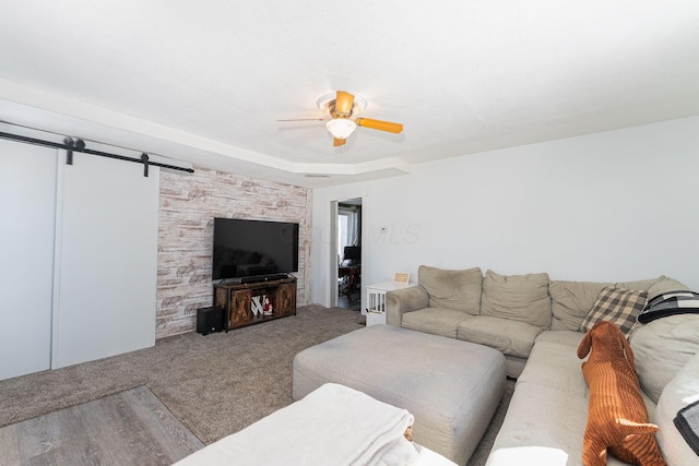 living room with ceiling fan, a barn door, and carpet flooring