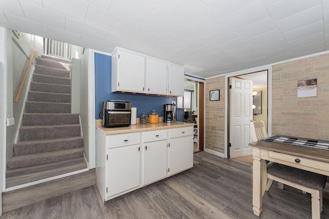 kitchen featuring white cabinets, dark hardwood / wood-style flooring, and brick wall