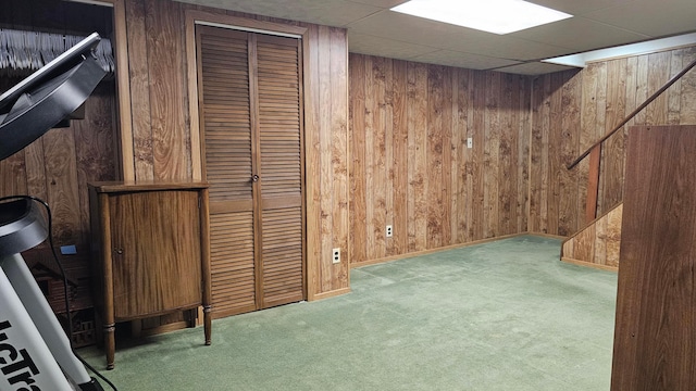 basement featuring a paneled ceiling, carpet flooring, and wood walls