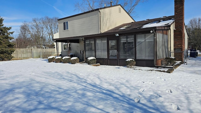 snow covered rear of property featuring a sunroom