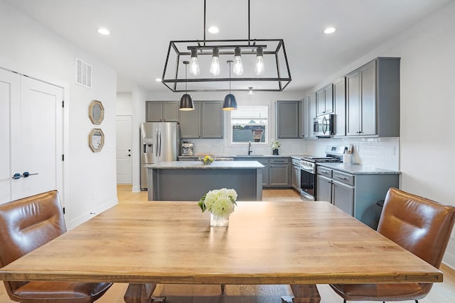 kitchen with sink, gray cabinets, backsplash, stainless steel appliances, and a kitchen island