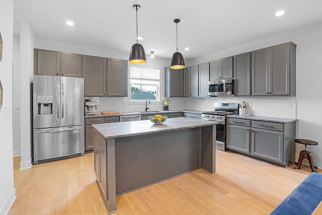 kitchen with sink, hanging light fixtures, light wood-type flooring, appliances with stainless steel finishes, and a kitchen island