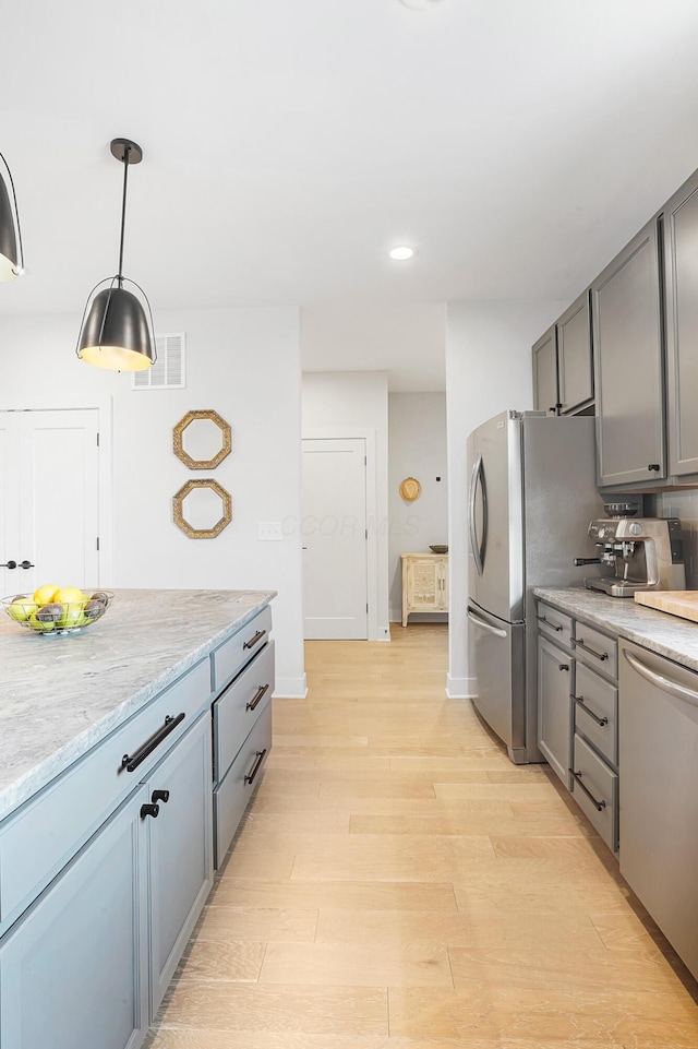 kitchen with decorative light fixtures, gray cabinetry, stainless steel appliances, light stone countertops, and light wood-type flooring