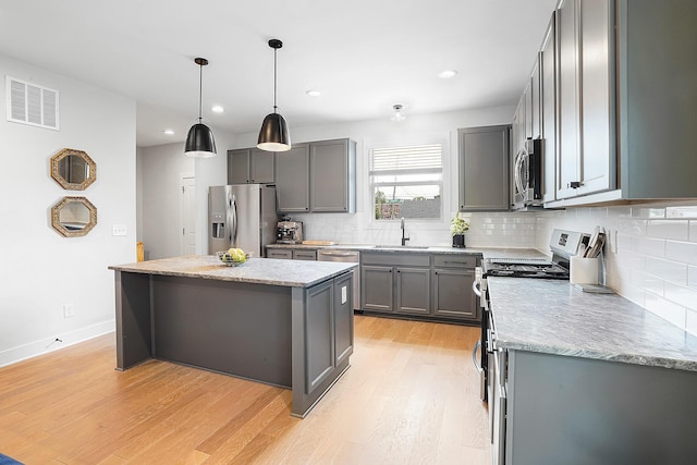 kitchen featuring a center island, hanging light fixtures, appliances with stainless steel finishes, gray cabinets, and light hardwood / wood-style floors