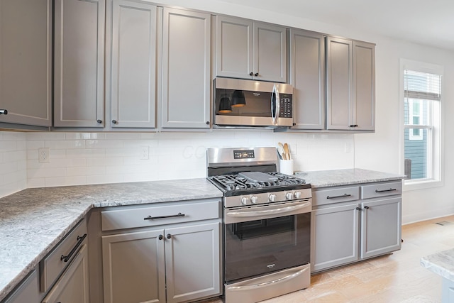 kitchen with light stone counters, stainless steel appliances, gray cabinets, and tasteful backsplash