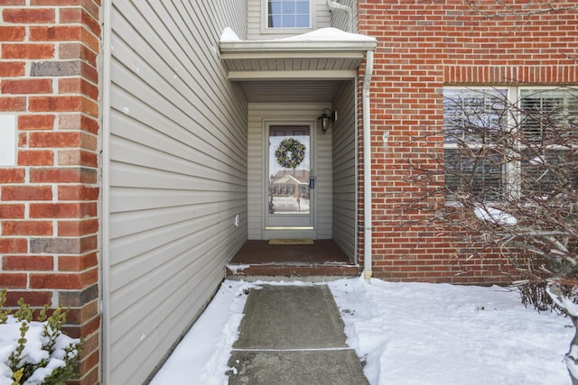 snow covered property entrance featuring brick siding