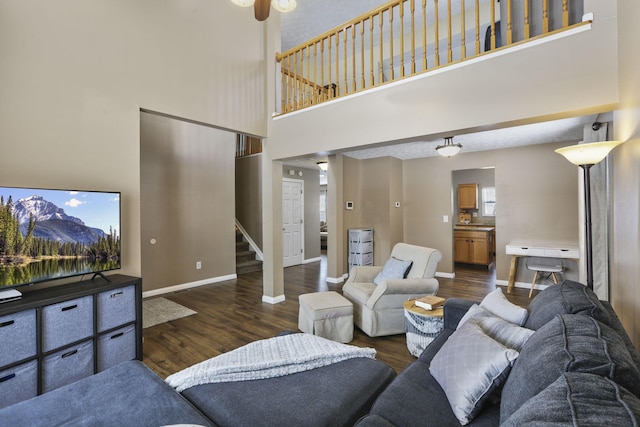 living room featuring dark wood-style flooring, a high ceiling, baseboards, and stairs