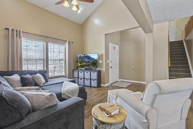 living room featuring stairway, ceiling fan, wood finished floors, high vaulted ceiling, and baseboards