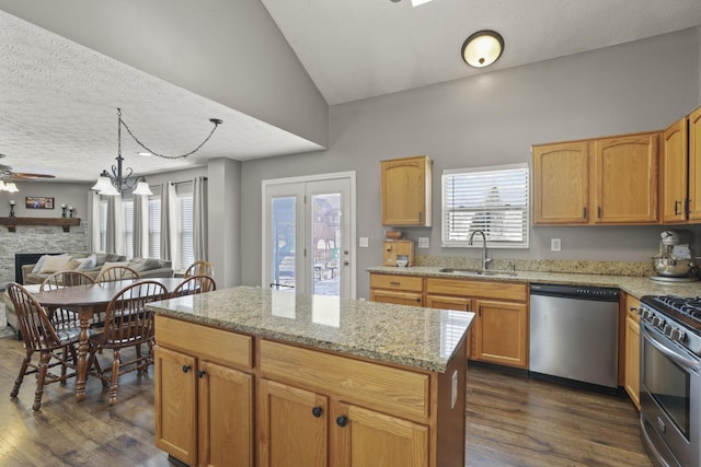 kitchen featuring dark wood finished floors, stainless steel appliances, open floor plan, a sink, and a stone fireplace