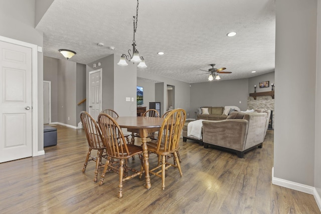 dining area featuring a stone fireplace, dark wood finished floors, a textured ceiling, and baseboards