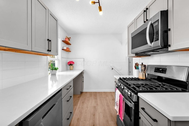 kitchen with light wood-type flooring, gray cabinetry, stainless steel appliances, backsplash, and a textured ceiling