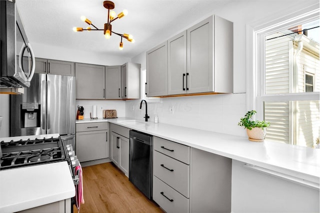 kitchen with appliances with stainless steel finishes, gray cabinetry, light hardwood / wood-style floors, backsplash, and sink