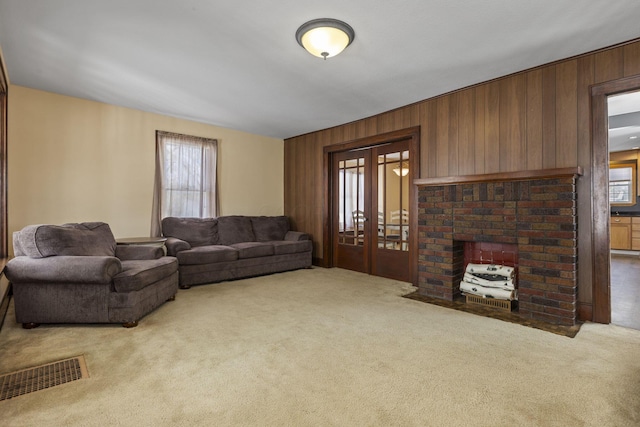 living room featuring wood walls, carpet, french doors, and a brick fireplace