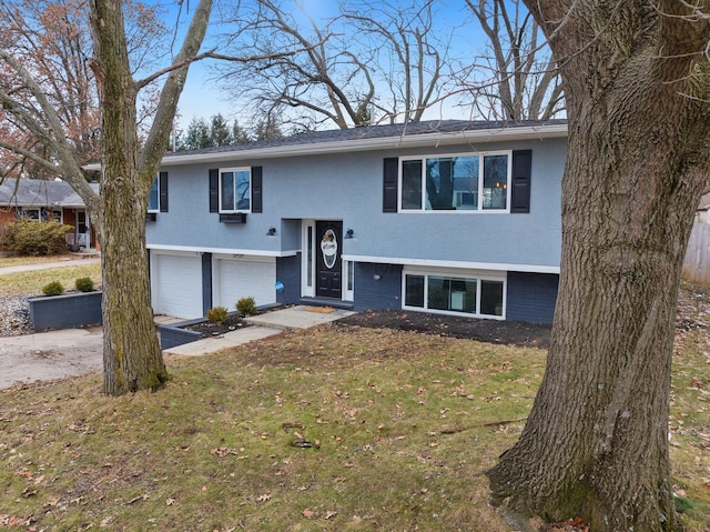 split foyer home with driveway, a garage, stucco siding, a front lawn, and brick siding