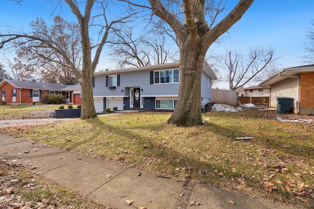 raised ranch featuring a garage, brick siding, fence, driveway, and a front lawn