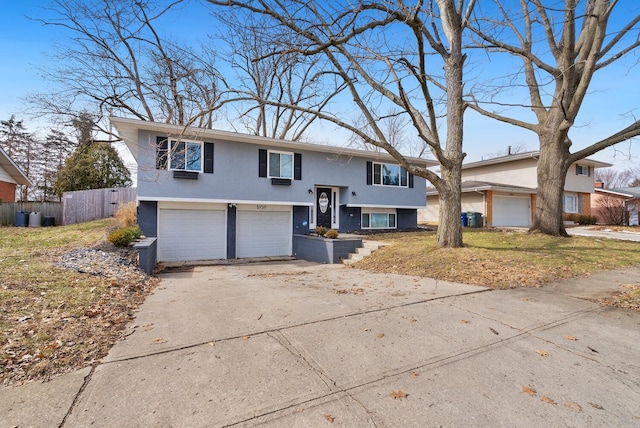 bi-level home featuring driveway, an attached garage, fence, and stucco siding