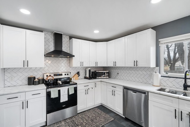 kitchen featuring stainless steel appliances, wall chimney range hood, a sink, and white cabinetry