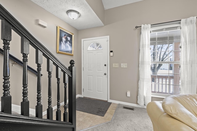 entryway featuring a textured ceiling, light tile patterned floors, visible vents, baseboards, and stairway