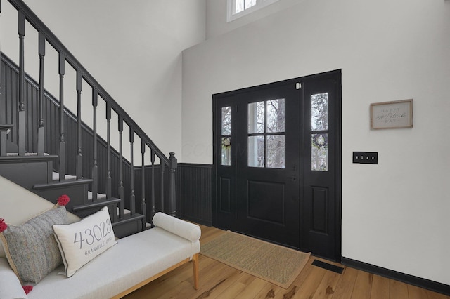 foyer entrance with visible vents, wainscoting, wood finished floors, a high ceiling, and stairs