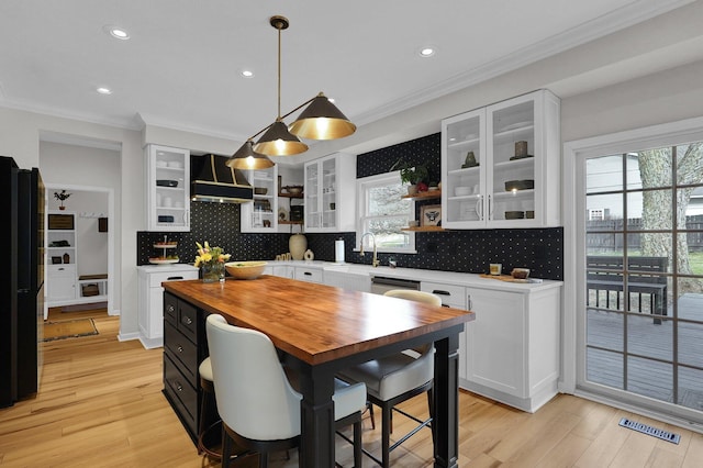 kitchen with white cabinets, light wood finished floors, wooden counters, and exhaust hood