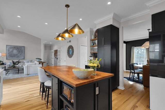 kitchen with dark cabinets, butcher block counters, open floor plan, and light wood finished floors