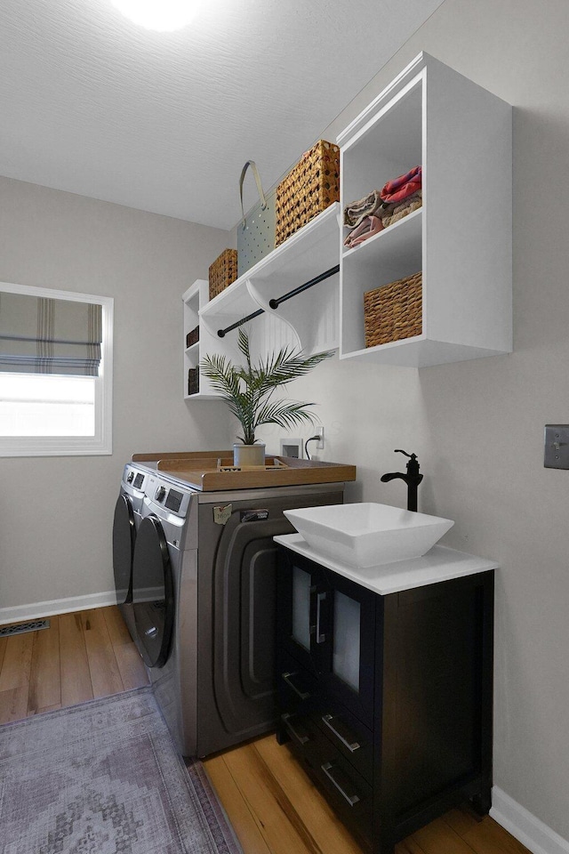 washroom with a sink, separate washer and dryer, wood finished floors, laundry area, and baseboards