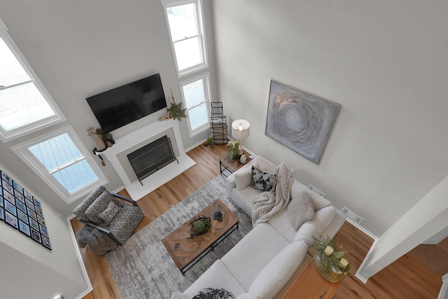 living room featuring a fireplace with flush hearth, a high ceiling, visible vents, and wood finished floors