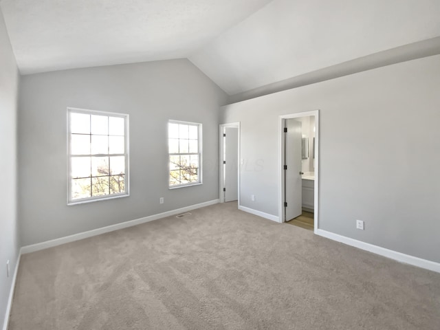 unfurnished bedroom with light colored carpet, vaulted ceiling, ensuite bath, and baseboards