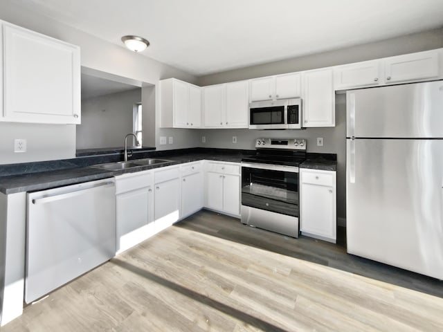 kitchen with stainless steel appliances, light wood finished floors, a sink, and white cabinets