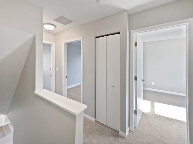 hall featuring light carpet, an upstairs landing, visible vents, and baseboards