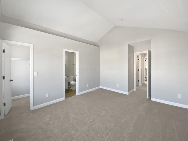 unfurnished bedroom featuring carpet floors, a closet, a spacious closet, vaulted ceiling, and baseboards