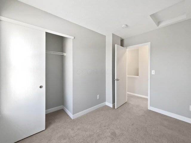 unfurnished bedroom with baseboards, a closet, attic access, and light colored carpet