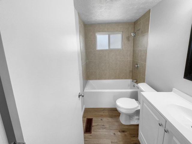 full bathroom featuring tiled shower / bath combo, toilet, wood-type flooring, a textured ceiling, and vanity