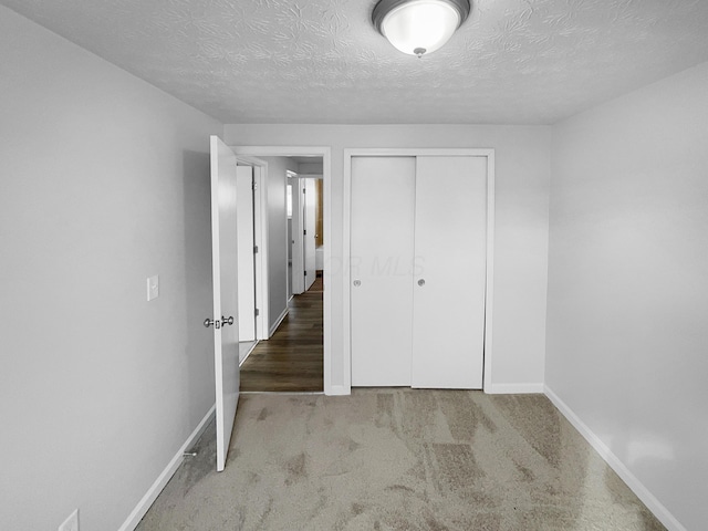 unfurnished bedroom with a closet, a textured ceiling, and light colored carpet