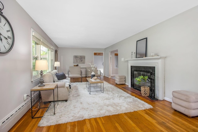 living room with a baseboard heating unit, wood finished floors, a fireplace, and baseboards