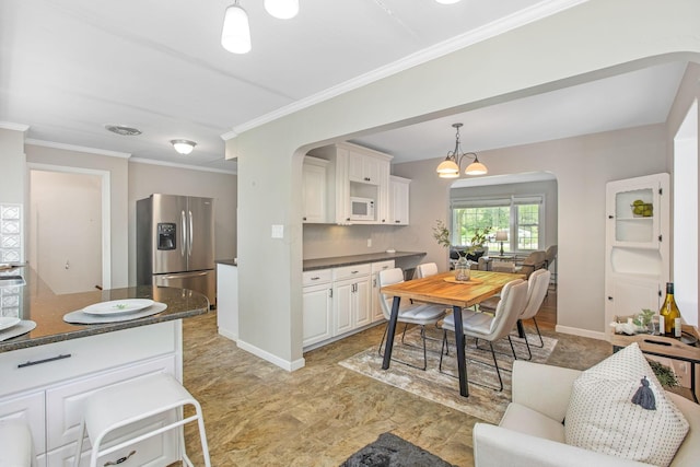 kitchen featuring dark countertops, stainless steel fridge, white microwave, arched walkways, and crown molding