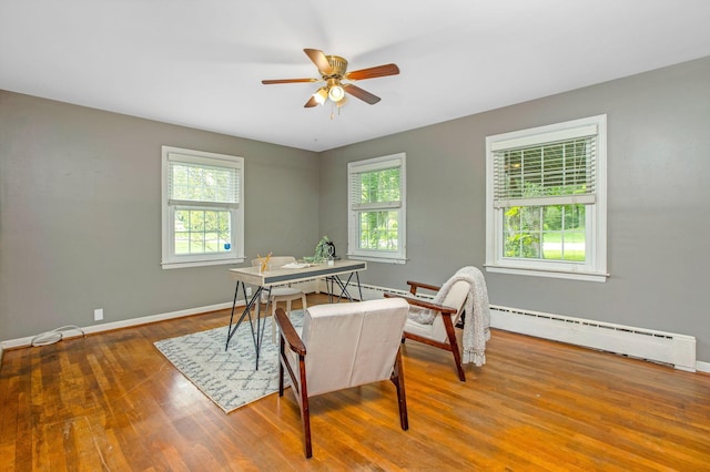 office featuring a baseboard heating unit, healthy amount of natural light, wood finished floors, and a ceiling fan