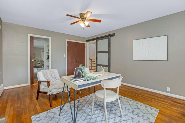 office area with a barn door, baseboards, ceiling fan, and wood finished floors